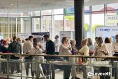 Uczestnicy konferencji podczas przerwy, ludzie stoją przy stołach z poczęstunkiem i rozmawiają w grupach w jasnym holu.