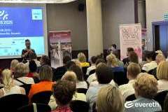 Zdjęcie przedstawia konferencję medyczną, prelegent mówi przez mikrofon i pokazuje slajd, uczestnicy siedzą i słuchają prezentacji.