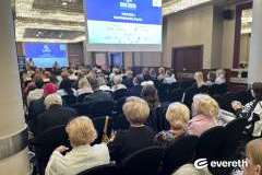 Zdjęcie przedstawia konferencję medyczną, prelegent mówi przez mikrofon i pokazuje slajd, uczestnicy siedzą i słuchają prezentacji.