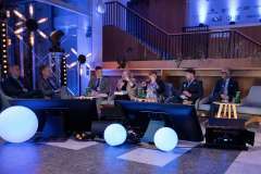 dwie kobiety i pięciu mężczyzn siedzi na fotelach i rozmawia, trzy osoby trzymają mikrofon