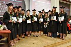 Grupa studentek ubranych w togi oraz biretki stoi w półokręgu i trzyma w rękach dyplomy i róże