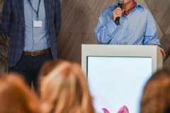 uczestnicy konferencji słuchają kobiety stojącej przy mównicy, obok niej stoi mężczyzna