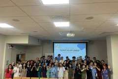 Grupa uczestników warsztatów w sali wykładowej, stojących przed ekranem rzutnika wyświetlającym napis NIME