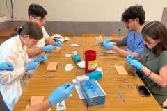 Młode osoby siedzące przy stole wykonujące ćwiczenia szycia na zwierzęcej skórze