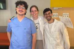 Jedna młoda kobieta i dwóch mężczyzn uśmiechnięci stoją na korytarzu w ubraniach medycznych