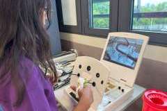 Młoda kobieta z długimi włosami w fartuchu lekarskim w trakcie ćwiczeń laparoskopem