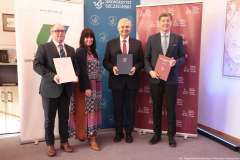 Jedna kobieta i trzech mężczyzn stoją przed ściankami ZUT, Uniwersytetu Szczecińskiego i PUM, prezentując podpisane dokumenty współpracy