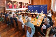 kilkanaście osób siedzi przy stole, w tle ścianka promocyjna Uniwersytetu Szczecińskiego i obrazy