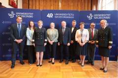 Grupa stojących osób na tle ścianki promocyjnej Uniwersytetu Szczecińskiego