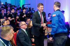 dwóch mężczyzn stojących w auli podają sobie rękę, obok i w tle pozostali uczestnicy spotkania